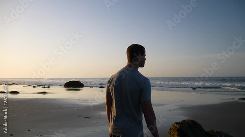 A strong man watching the ocean waves and stretching for a morning run and workout on the beach at sunrise in Santa Barbara, California SLOW MOTION. photo