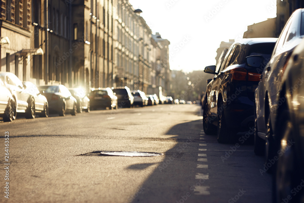 The city landscape is empty from the people of the street on which there are parked cars, illuminated by the rays of the sunset. The city landscape is empty from the people of the street on which there are parked cars, illuminated by the rays of the sunset.