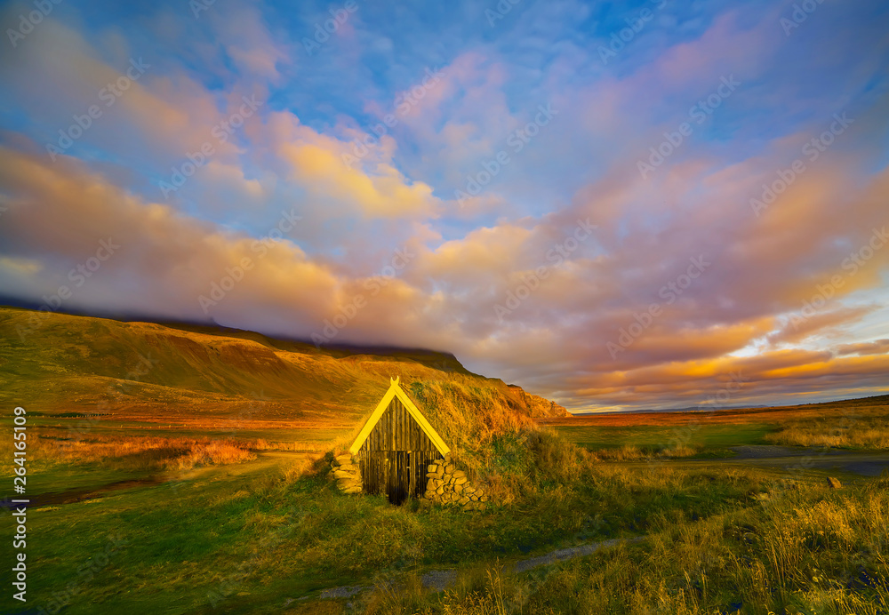 Dawn on the shore of the Atlantic Ocean. A traditional old house with a roof overgrown with grass on the beach. Iceland. Sea landscape. soft sunlight.