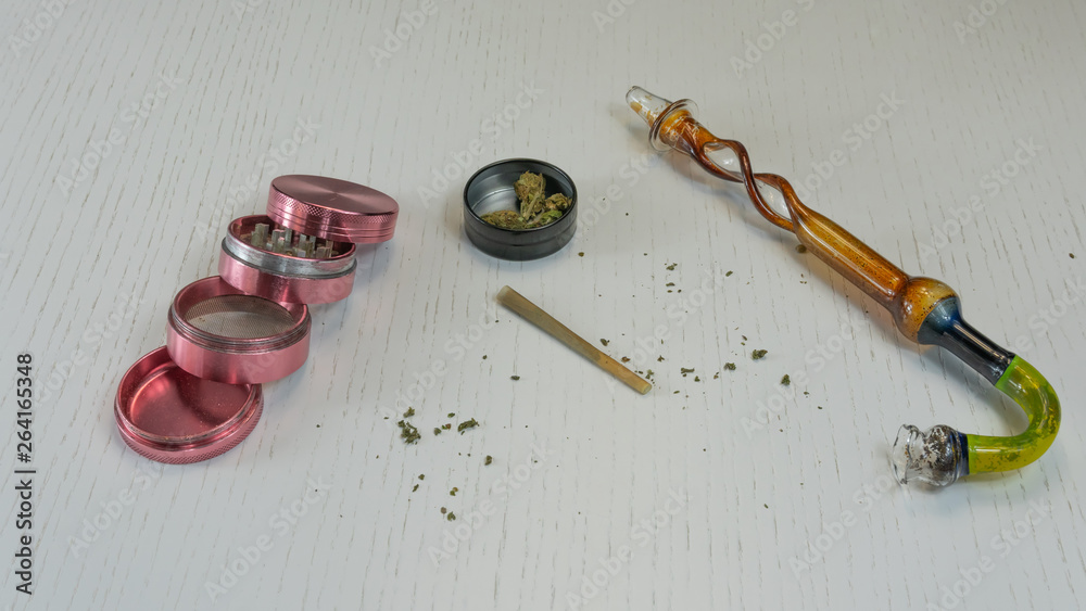 Marijuana joint, buds, grinder and smoking pipe are on the white table Marijuana joint, buds, grinder and smoking pipe are on the white table