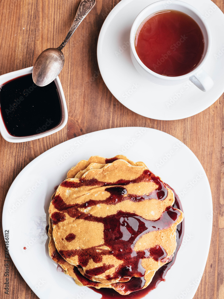Pancakes with cherry syrup. Tea. Wooden table.