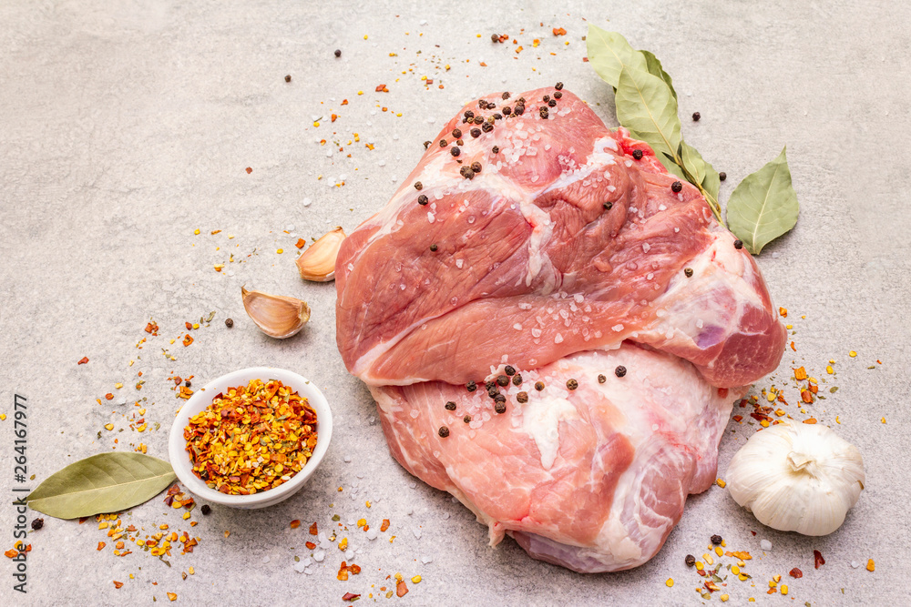 Raw pork shoulder with spices. Bay leaf, garlic. On a stone background, close up.