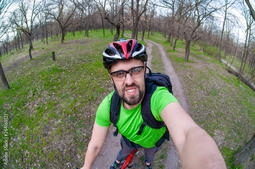 Smiling sports guy in bicycle helmet taking selfie in spring park