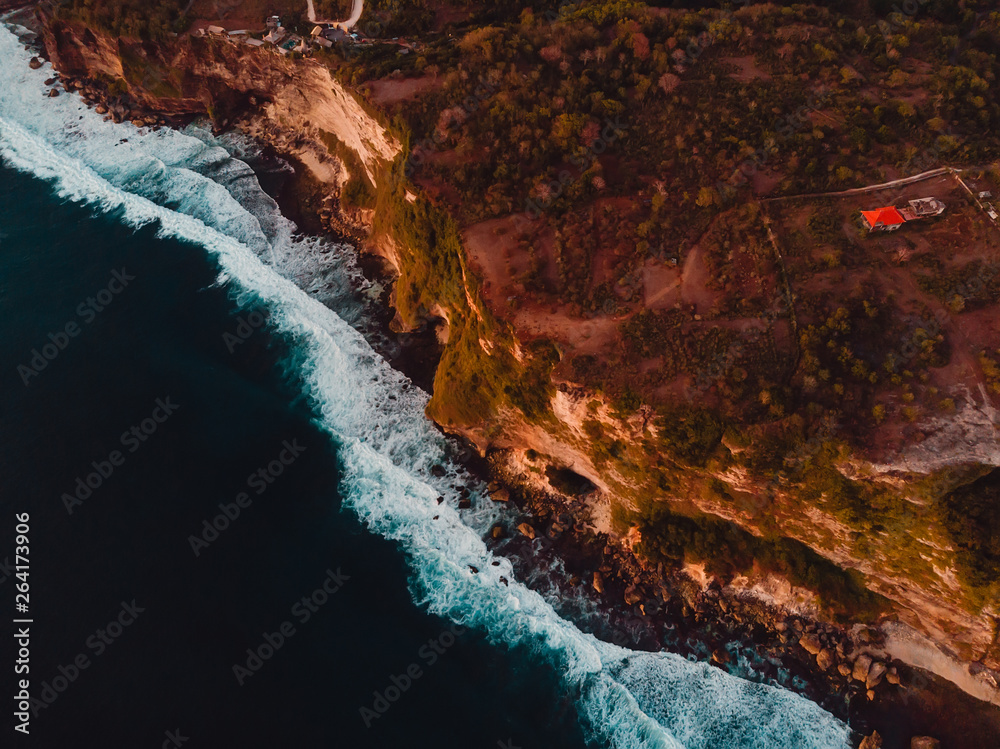 Aerial view of rocky shore with cliff and ocean warm sunset in Bali, Uluwatu.