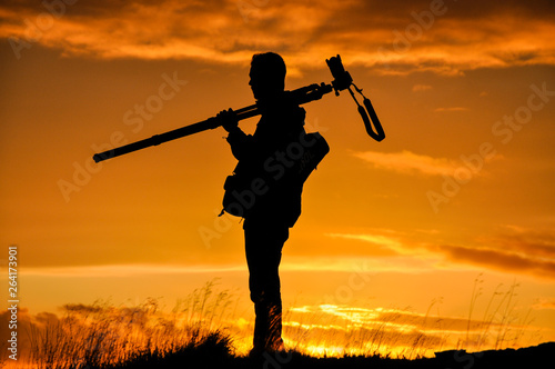 Silhouette of photographer with tripod against setting sun
