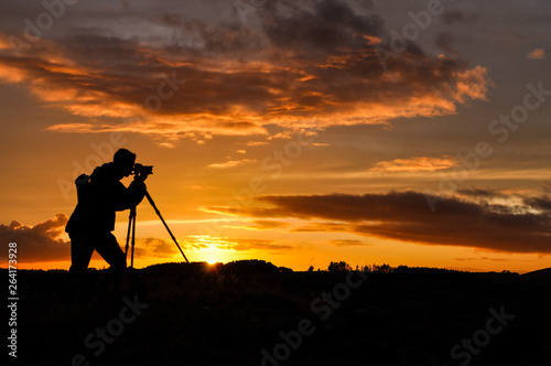 Silhouette of photographer with tripod against setting sun