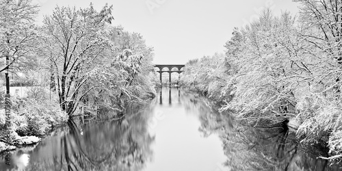 Snow capped trees reflecting on a river with viaduct in the background