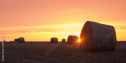 Sun shining between hay bales with orange sky