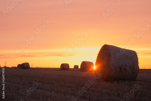 Sun shining between hay bales with orange sky