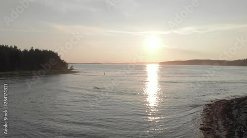 Cinematic drone / aerial footage rotating showing a surfer swimming in the water in the coast of Kingsburg, Nova Scotia, Canada during summer season - sunset time. photo