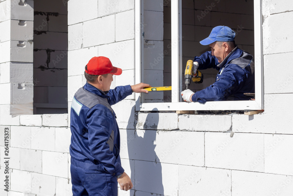 workers install glazing in a house under construction, make measurements, drill, saw grinder workers install glazing in a house under construction, make measurements, drill, saw grinder