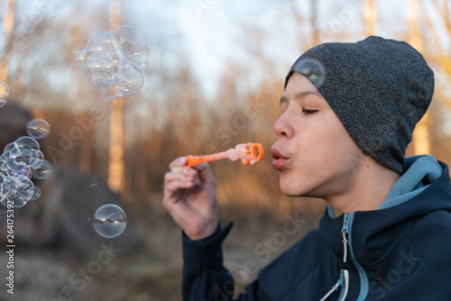 teen boy in blue jacket and grey hat blowing bubbles in Park