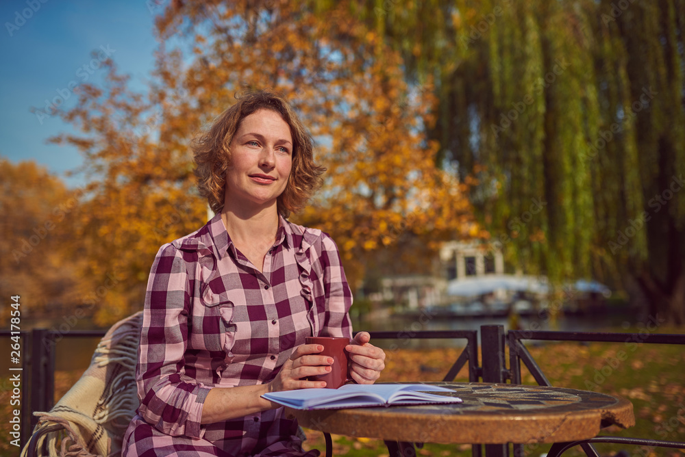 Pretty woman with mug and book in cafe in autumn park
Pretty woman with mug and book in cafe in autumn park