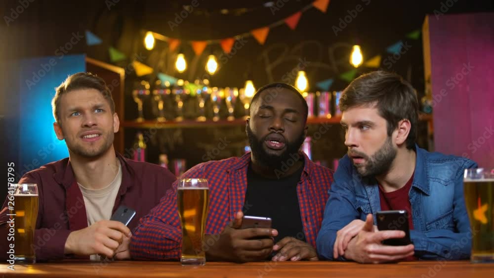 Multiethnic male friends watching football match in pub, upset with team losing Multiethnic male friends watching football match in pub, upset with team losing