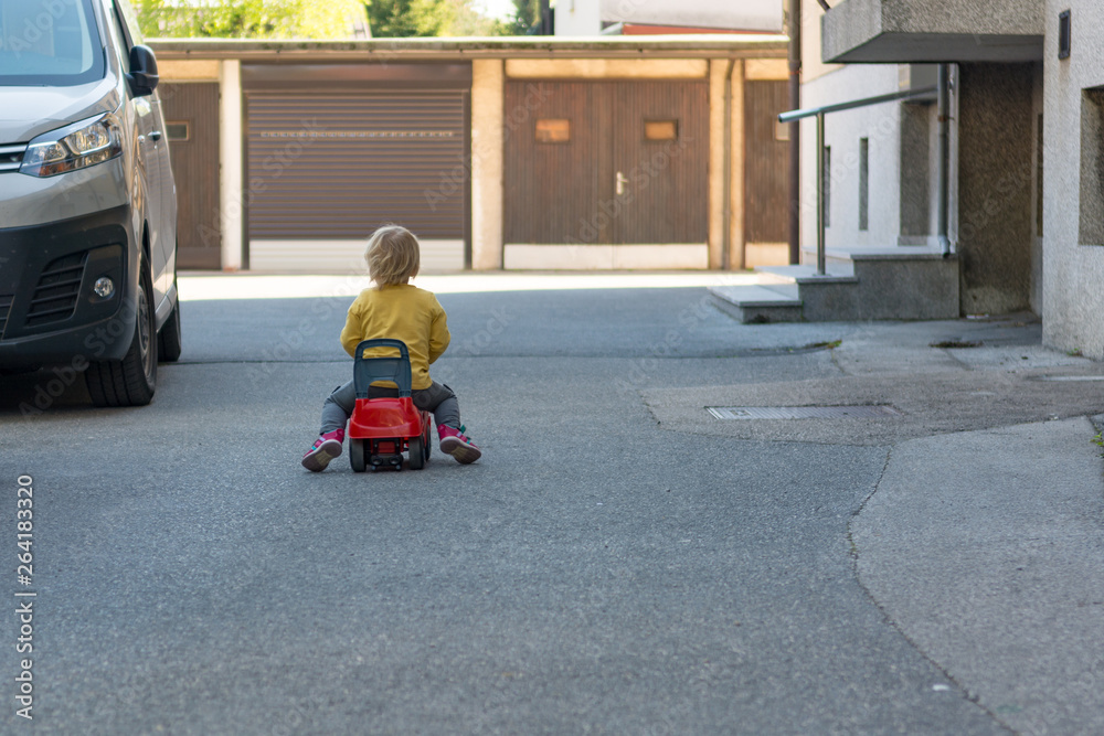 Small child playing outdoor racing her red plastic car. Small child playing outdoor racing her red plastic car.