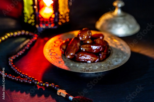 The Muslim feast of the holy month of Ramadan Kareem with dates on a tray on a dark background. Beautiful background with a shining lantern Fanus.