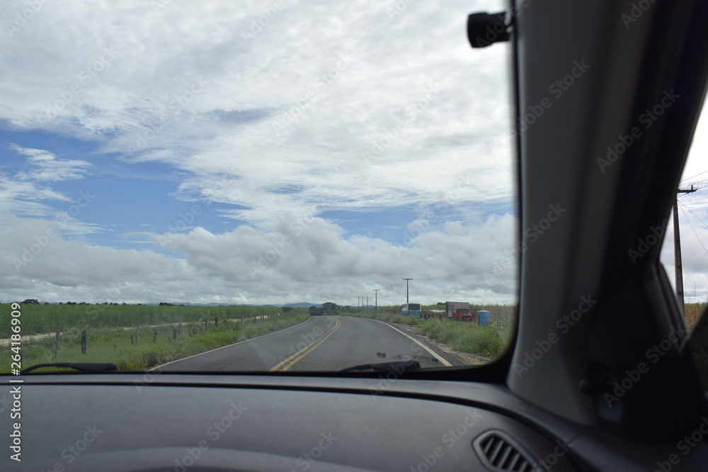 Estrada vista de dentro de um carro. Perspectiva, campo verde e céu azul.