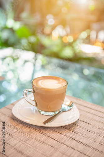 Hot coffee on the glass table over blurred garden background with vintage morning warm light
