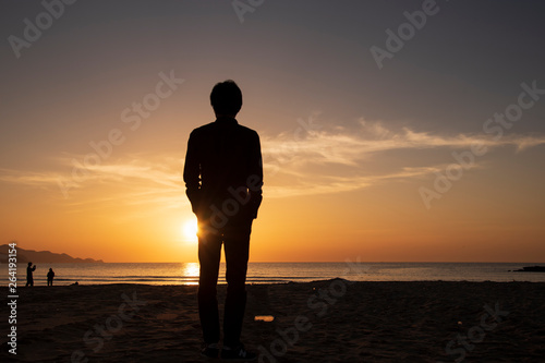 夕暮れの砂浜に立つ男性
