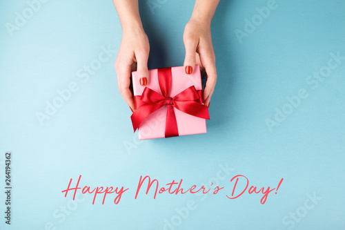 Female's hands holding gift box on blue background.