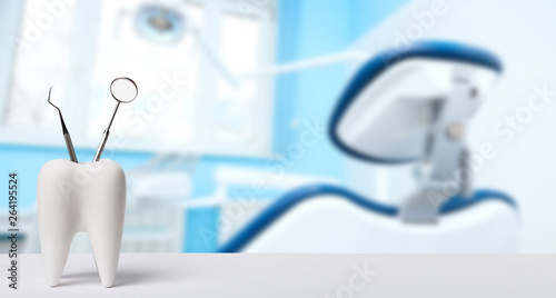 Oral dental hygiene. Healthy white tooth and dentist mirror with explorer probe instrument against blurred dentist Office background with dental chair and lamp. photo