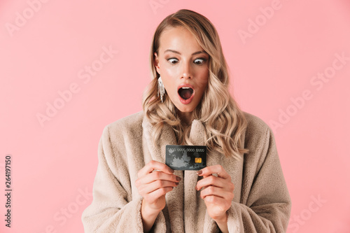 Shocked blonde woman wearing in fur coat holding credit card