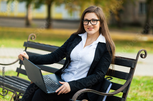 Business woman sitting in the park on a bench, working with a laptop