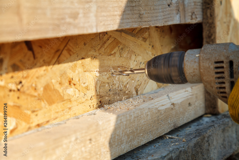 A worker drills a wooden beam with an electric drill A worker drills a wooden beam with an electric drill