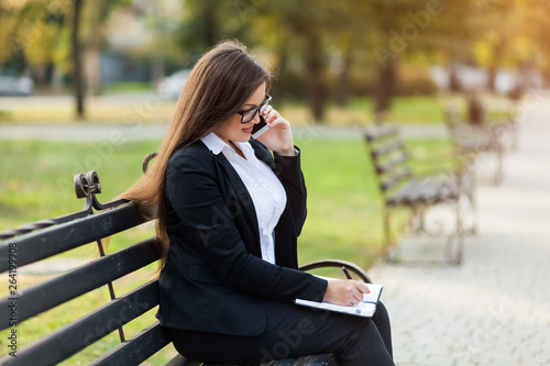 Happy businesswoman calling on mobile phone and taking notes outdoor