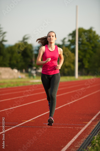 Beautiful young woman runner run on a track in early summer afternoon