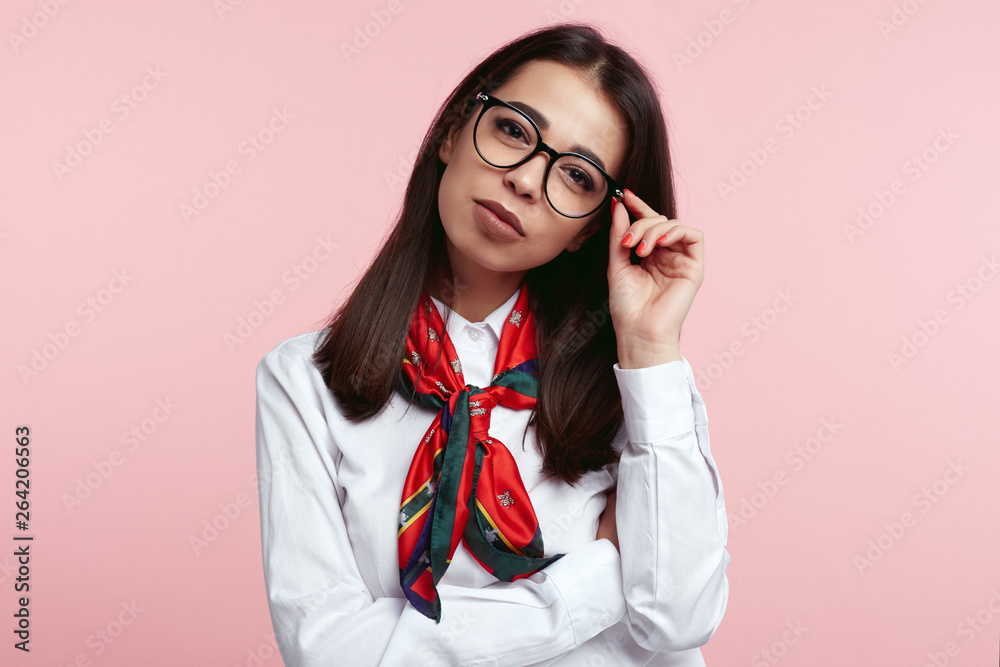 Young confident brunette business female wearing white shirt and scarf, holding her eyeglasses isolated over pink background. Young confident brunette business female wearing white shirt and scarf, holding her eyeglasses isolated over pink background.
