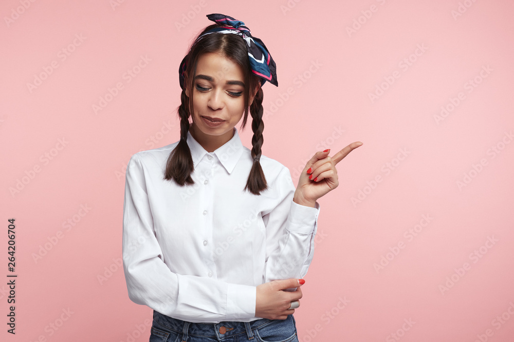 Attractive fashionable girl with closed eyes, pointing at right blank space, standing against pink background. Attractive fashionable girl with closed eyes, pointing at right blank space, standing against pink background.