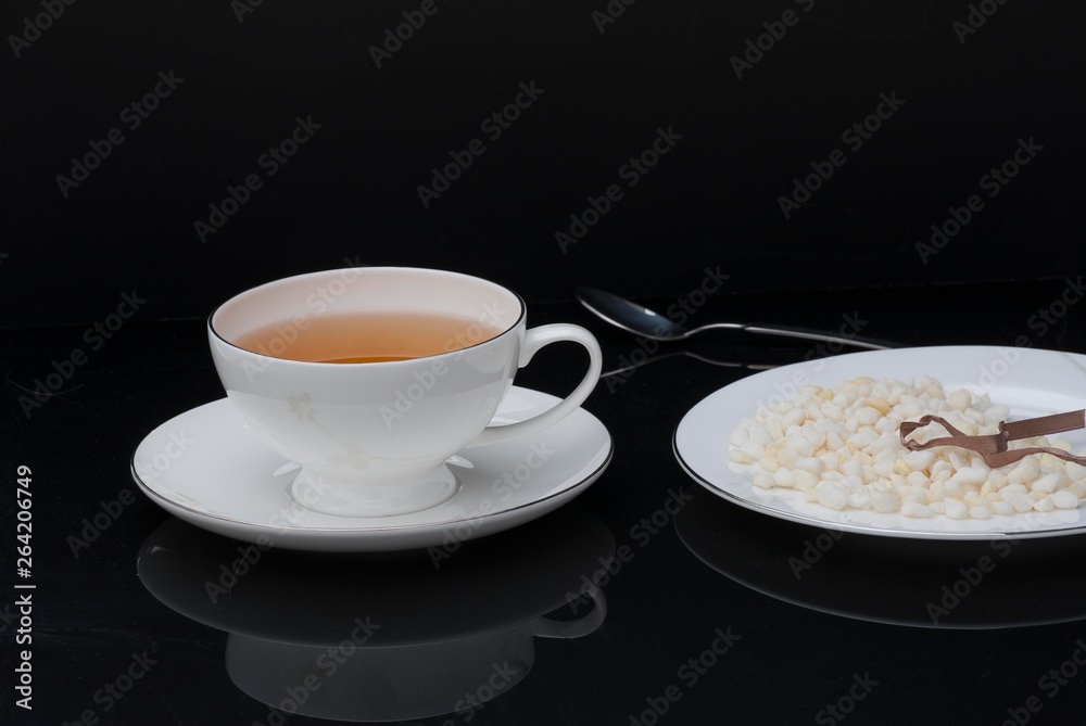 Granulated sugar in the shape of heart and cup of tea on black background Granulated sugar in the shape of heart and cup of tea on black background
