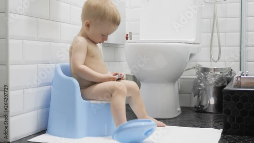 Little boy on the potty in bathroom is watching cartoons on smartphone, lifestyle.