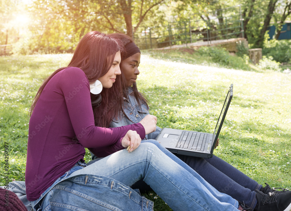 couple of multi-ethnic girls student sitting on the meadow couple of multi-ethnic girls student sitting on the meadow