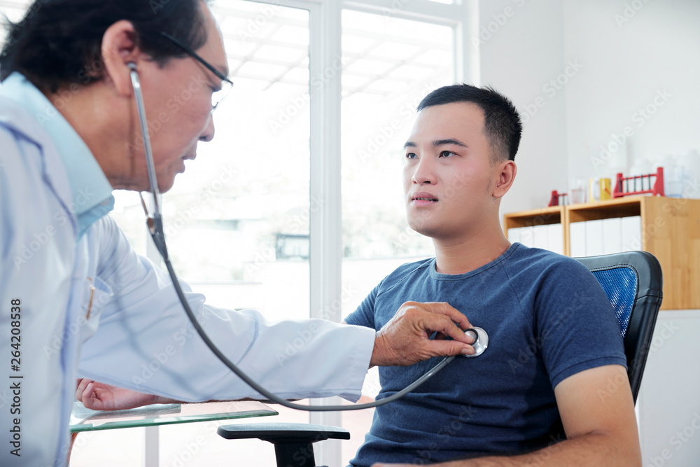 Fototapeta premium Doctor checking heartbeat of young man