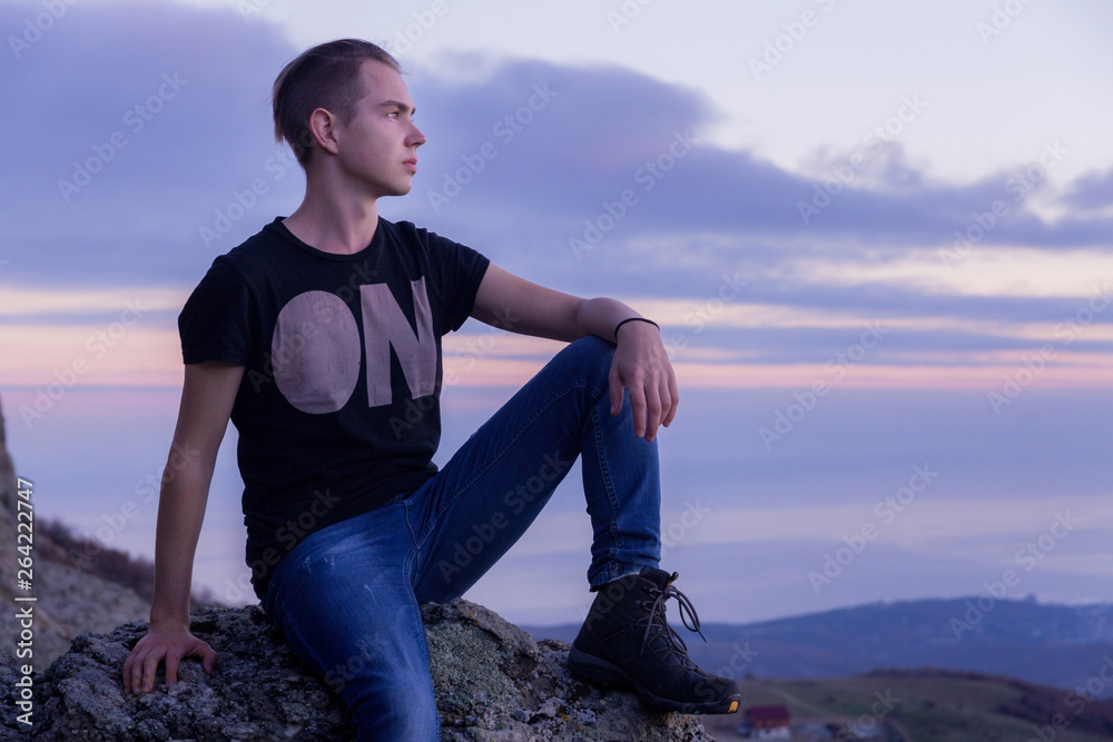 Young attractive man located with  on the top of mountains against the backdrop of a purple sunset, portrait in profile.