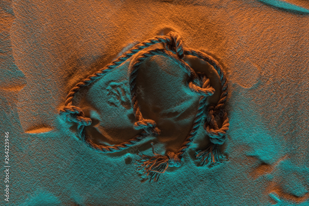 Naklejka premium top view of bend rope with knots on sand with orange and blue lights