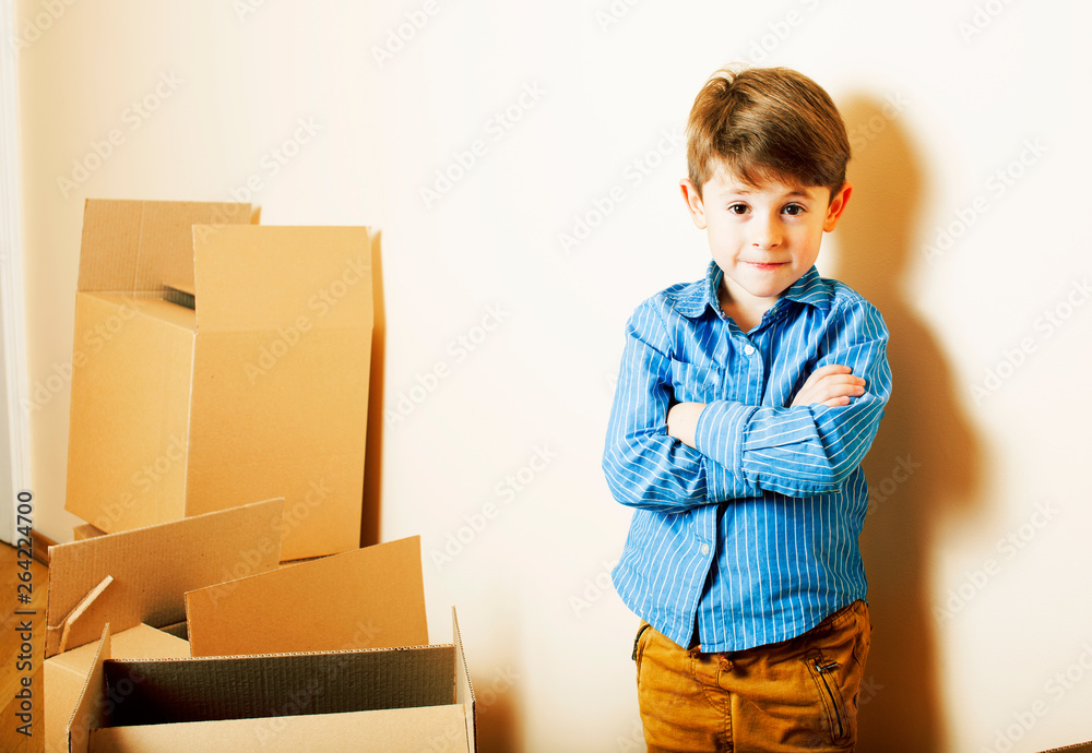 little cute boy in empty room, move to new house. home alone among boxes close up kid smiling, lifestyle real people concept