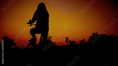 Long haired girl Sitting on a bike Staring at the sunset, silhouette concept.