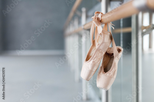 Pointe shoes hang on ballet barre in dance class room. Blurred background of ballet classic school.