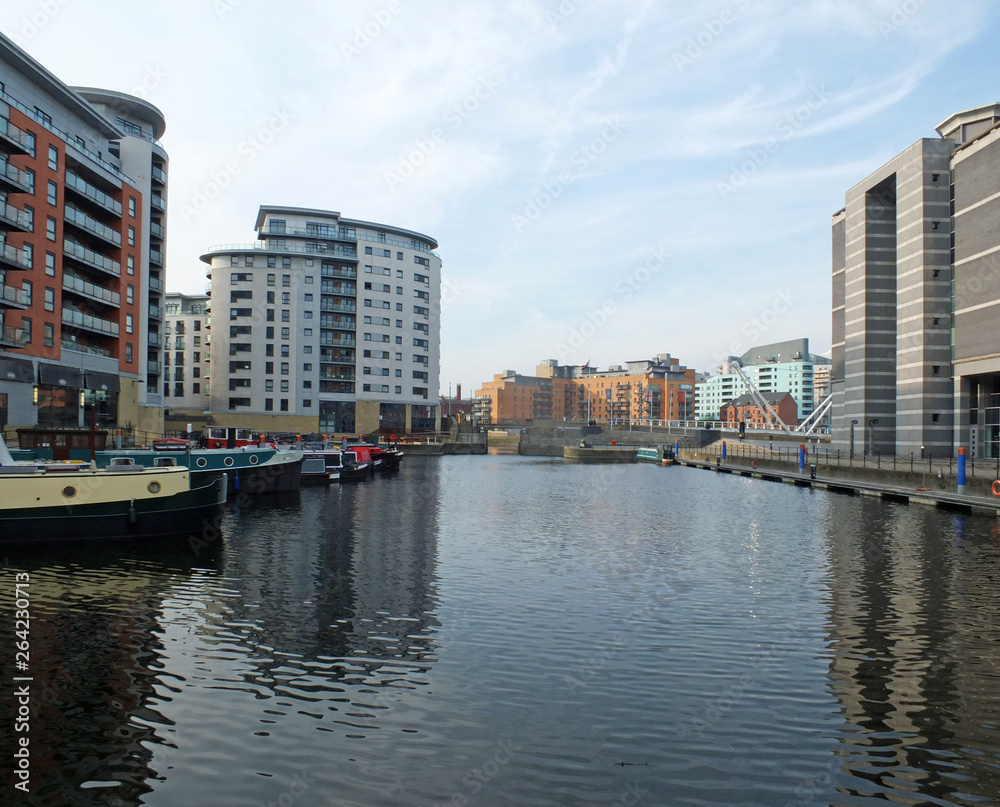 a view of clarence dock in leeds looking towards the lock and river with canal boats moored alongside apartment buildings and hotels reflected in the water