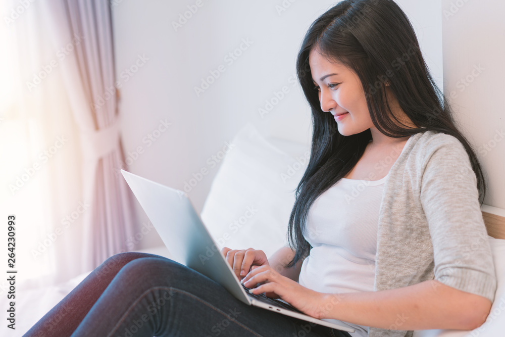 Young woman working on a laptop sitting on bed at home Young woman working on a laptop sitting on bed at home