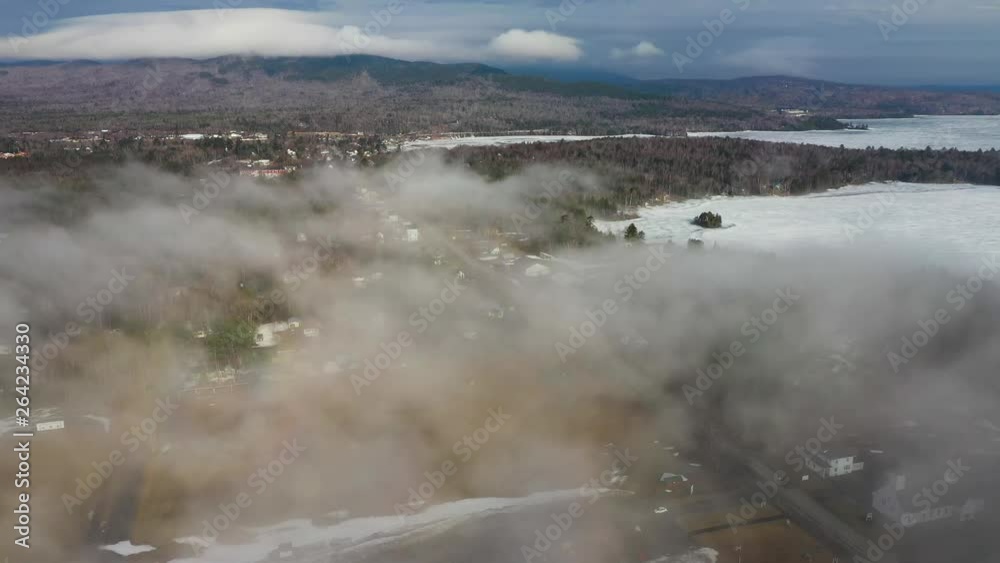 Stationary shot over a small rural town as fog rolls in from frozen lake on a spring morning AERIAL Stationary shot over a small rural town as fog rolls in from frozen lake on a spring morning AERIAL