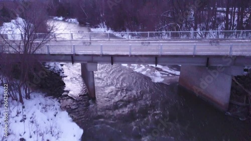 Drone shot over cold icy water on the Beaver river in The Blue Mountains, Ontario with cars going over a bridge. photo