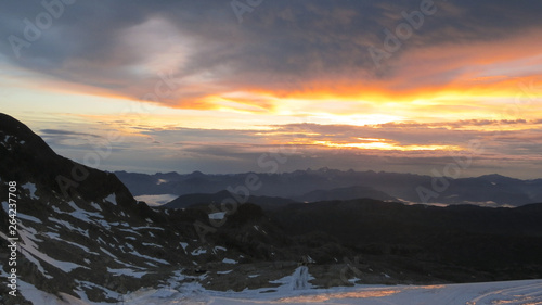 sunrise in the mountains with a rock formation and snow in the foreground and the colorful sky in yellow and orange in the background