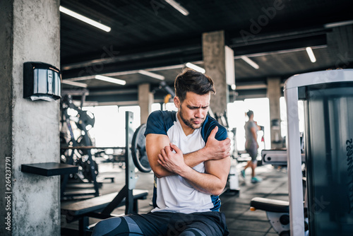 Portrait of an athlete feeling the pain in arm, while exercising in the gym.
