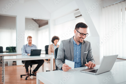 Smiling businessman in formal wear using laptop in modern shared office.