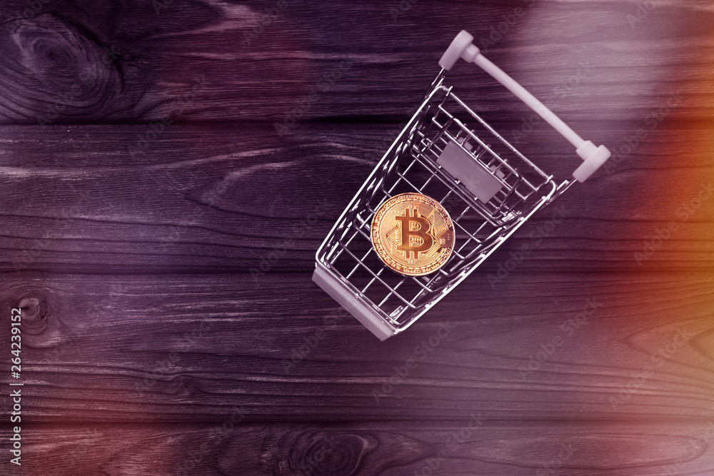 Bitcoin in the cart from the supermarket on the background of a wooden table. the Internet, a virtual currency. e-business.