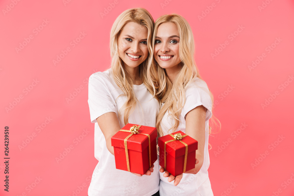 Smiling blonde twins wearing in t-shirts giving gift boxes
